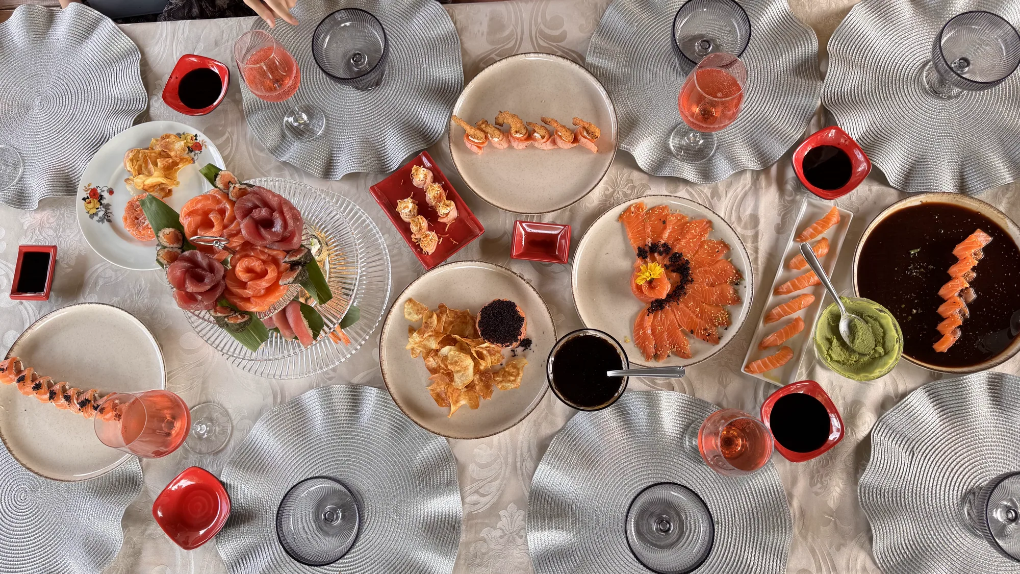 Mesa posta da Nami vista de cima: sashimis, niguiris, rosas de salmão e atum, ostras e taças de rosé